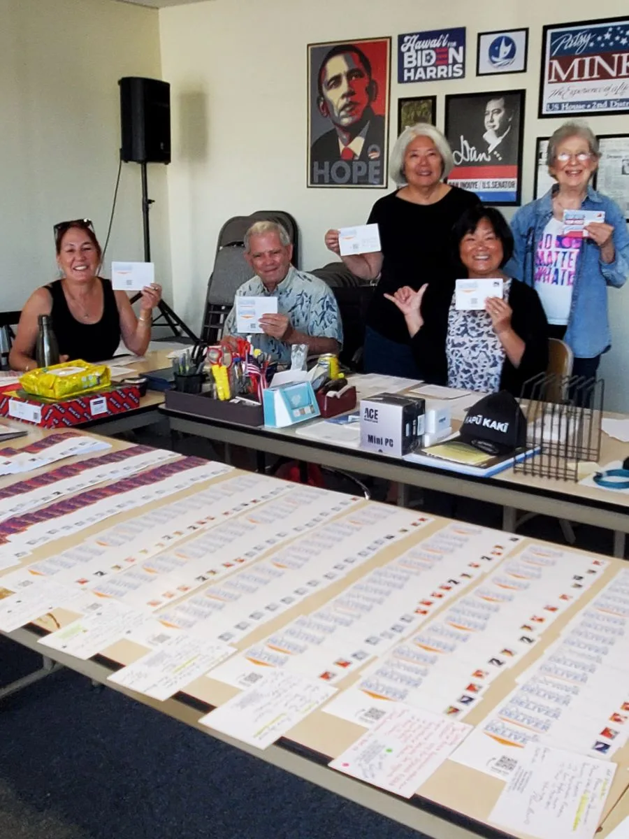 Group or indivisibles showing standing behind a table with hundreds of postcards, ready to be posted