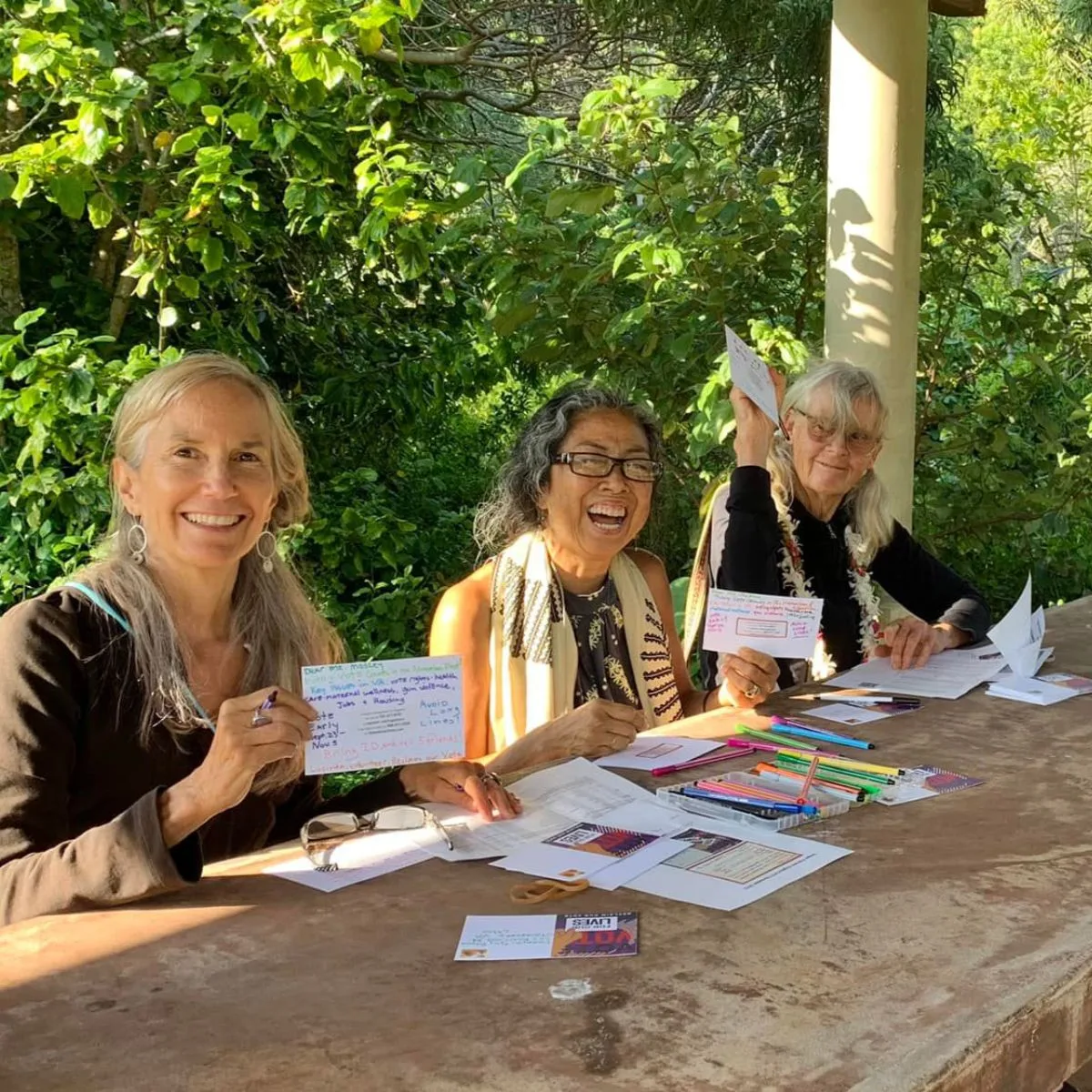 Group of people posing with their postcards at the weekly postcarding party in Kailua, hosted by the Blue Wave and Indivisible Windward Oahu.